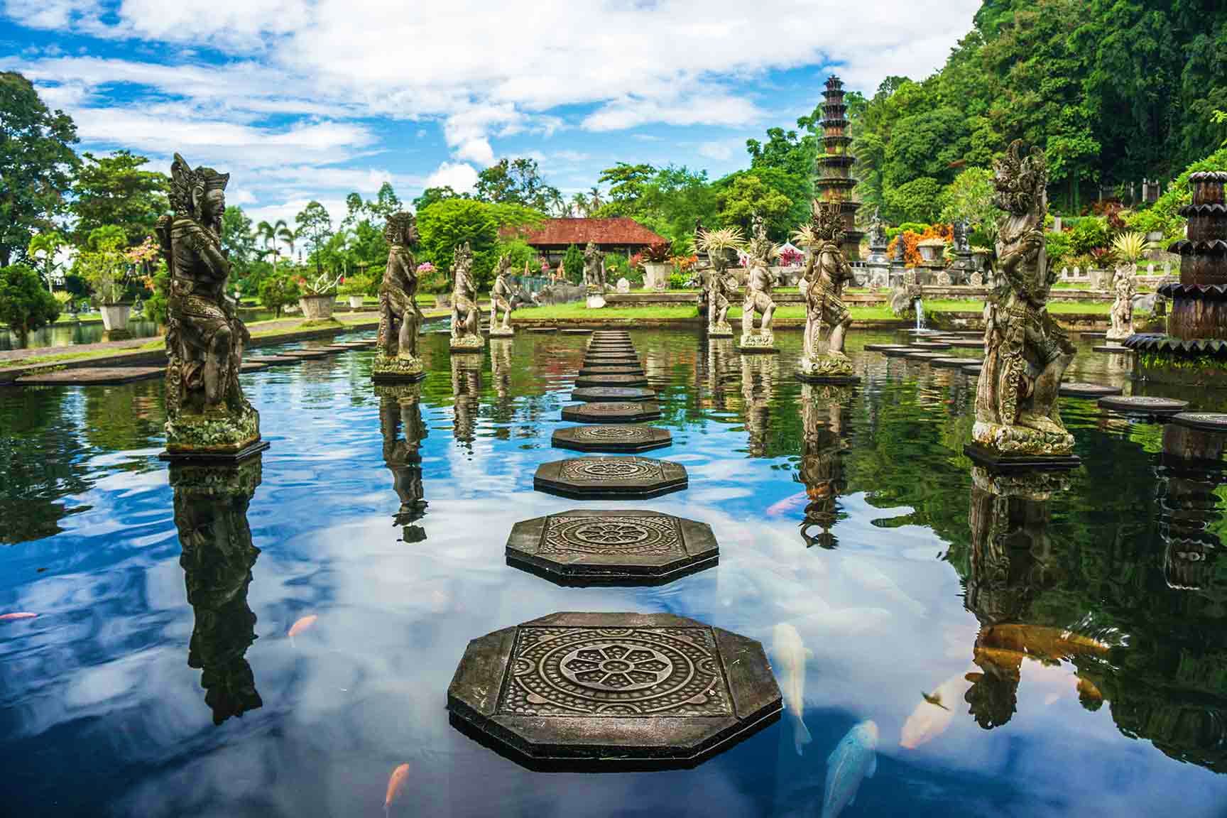 Indonesia Visa Ancient Hindu temple complex in Bali with ornate stone statues lining a reflecting pool pathway and traditional architecture